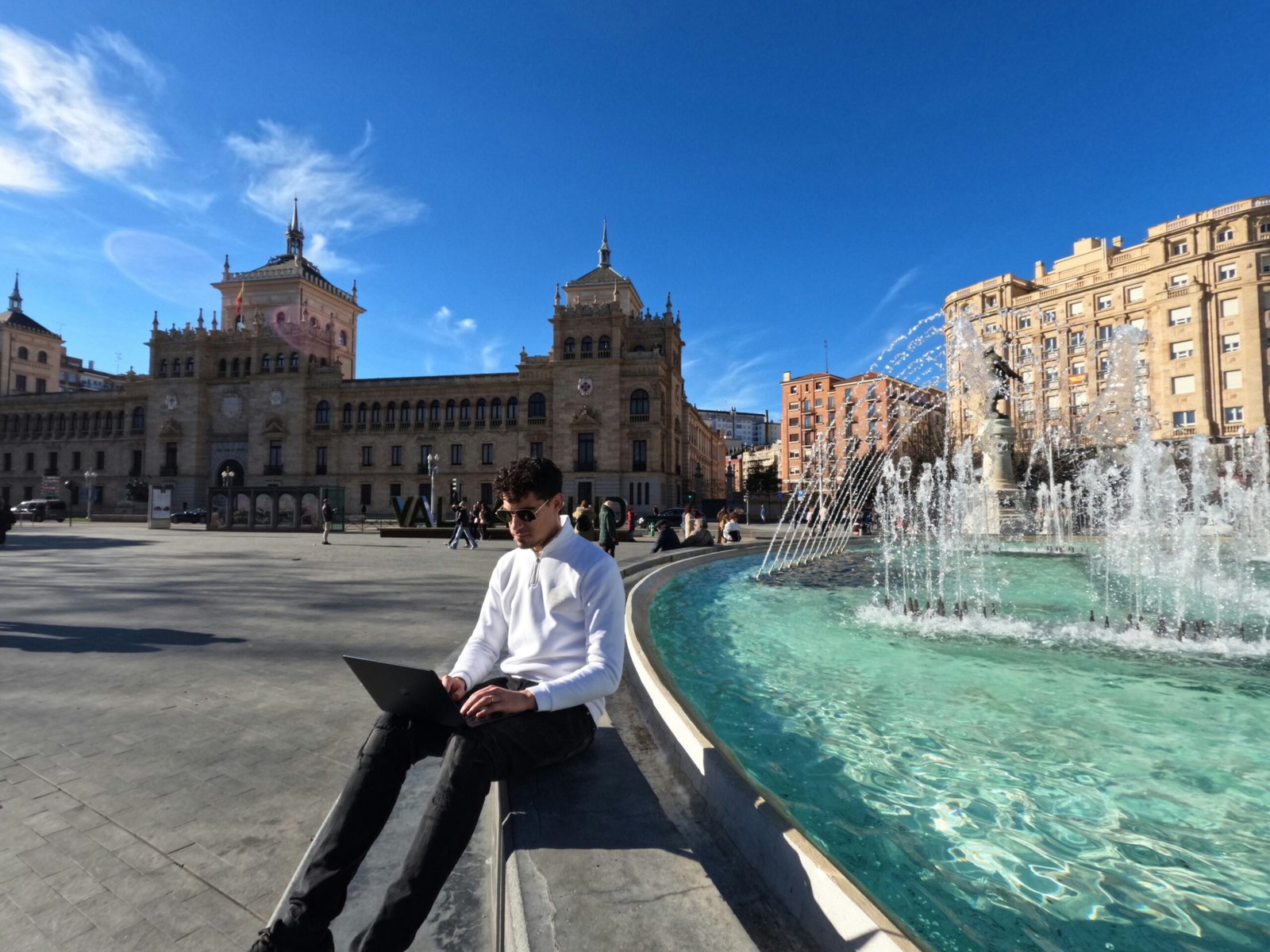 Man working on computer next to fountain in Spain.