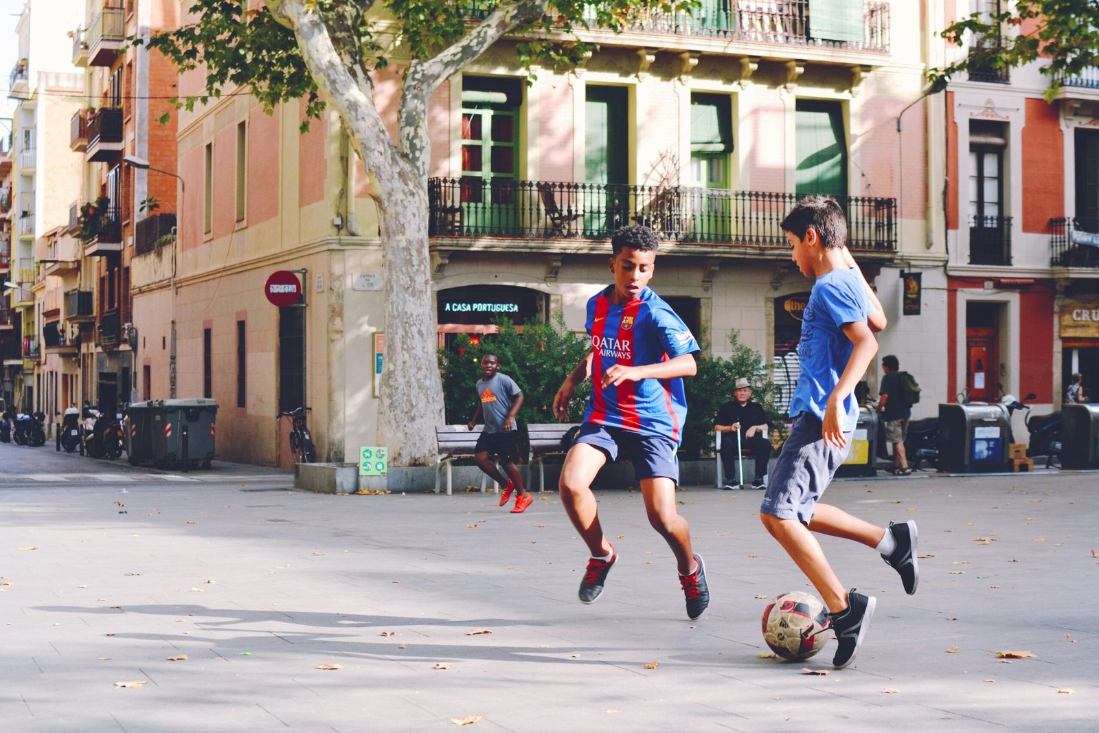Two children in Barcelona jerseys playing soccer in a plaza.